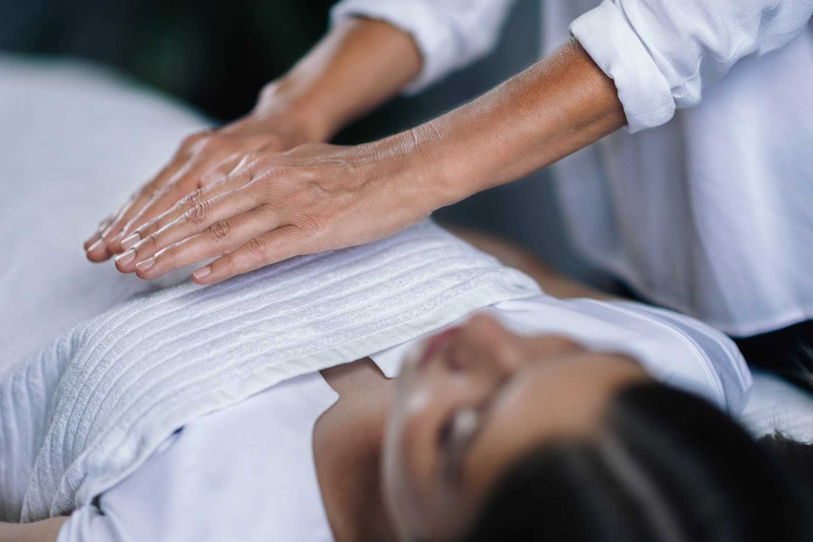 Reiki Healing Treatment Horizontal image of female Reiki therapist holding hands over patient chest healing heart chakra. Peaceful beautiful teenage girl lying with her eyes closed.